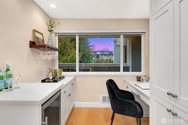 home office with a dry bar, light wood-type flooring, baseboards, visible vents, and beverage cooler