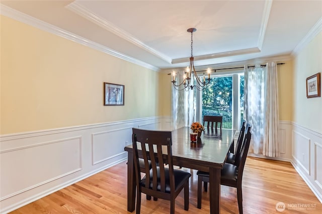 dining area with a decorative wall, a notable chandelier, light wood-style floors, and a raised ceiling