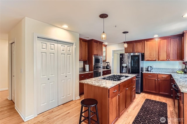 kitchen featuring light stone counters, stainless steel appliances, light wood finished floors, and a kitchen island