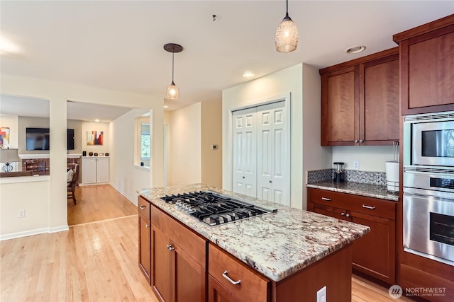 kitchen with light stone countertops, light wood finished floors, pendant lighting, and stainless steel appliances