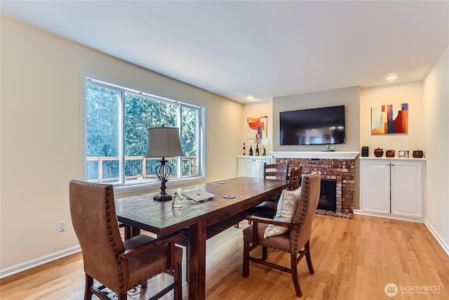 dining room featuring light wood-style floors, a brick fireplace, and baseboards