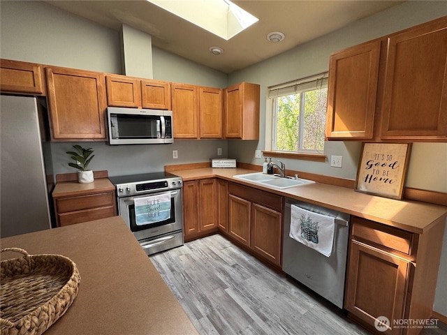 kitchen with light wood finished floors, a sink, stainless steel appliances, lofted ceiling with skylight, and light countertops