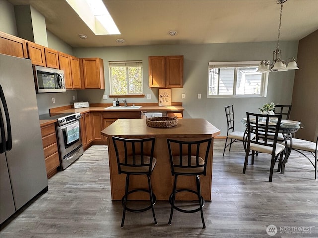 kitchen featuring a sink, stainless steel appliances, a center island, an inviting chandelier, and light wood finished floors