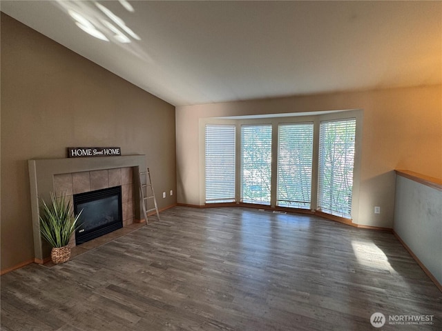 unfurnished living room featuring a tiled fireplace, baseboards, wood finished floors, and lofted ceiling