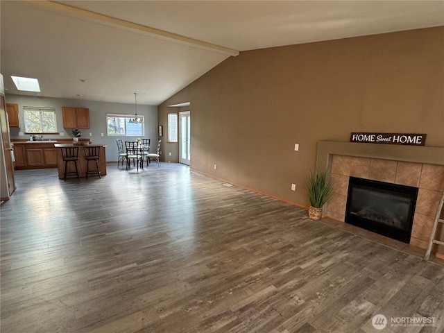 living area with a fireplace, dark wood-type flooring, baseboards, and lofted ceiling with skylight