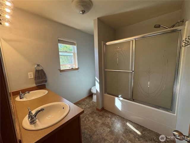 full bathroom with toilet, double vanity, a sink, and bath / shower combo with glass door