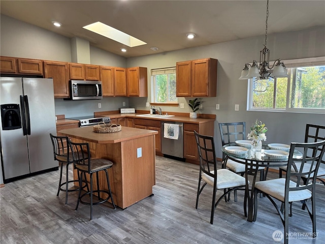 kitchen featuring a sink, a center island, a breakfast bar, light wood-style flooring, and appliances with stainless steel finishes