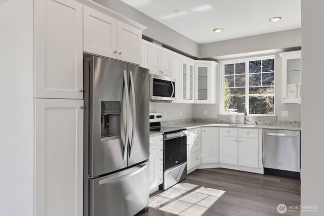 kitchen with white cabinets, a sink, light stone countertops, glass insert cabinets, and appliances with stainless steel finishes
