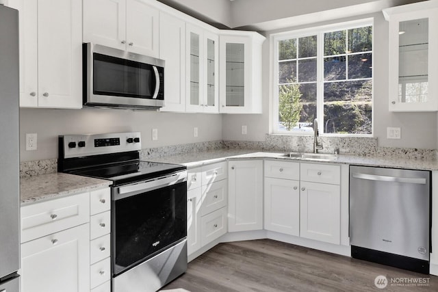 kitchen with stainless steel appliances, a sink, white cabinetry, wood finished floors, and light stone counters