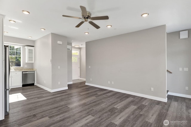 unfurnished living room featuring ceiling fan, a wealth of natural light, dark wood-style flooring, and baseboards
