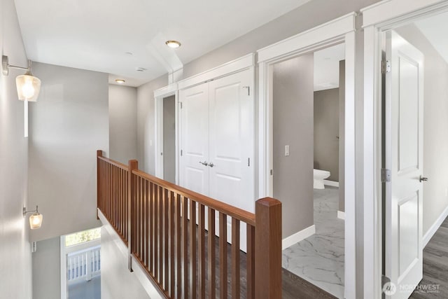 hall with marble finish floor, baseboards, and an upstairs landing