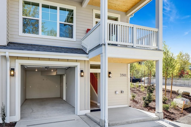 view of exterior entry featuring roof with shingles, a balcony, and a garage