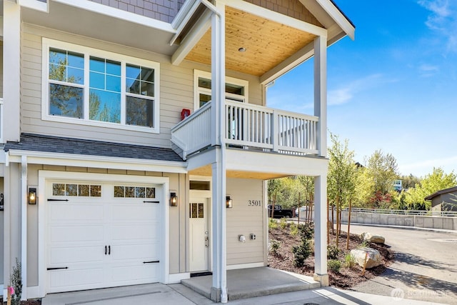 entrance to property with fence, a balcony, roof with shingles, and a garage