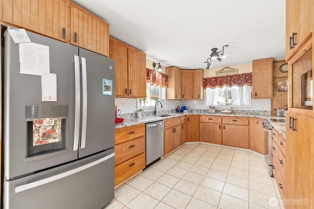 kitchen featuring backsplash, light stone countertops, appliances with stainless steel finishes, and a sink