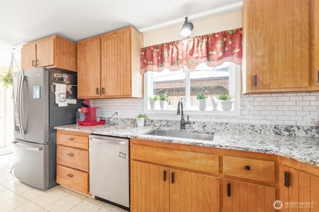 kitchen featuring stainless steel appliances, a sink, light tile patterned flooring, decorative backsplash, and light stone countertops