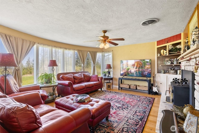 living room featuring wood finished floors, visible vents, a textured ceiling, built in shelves, and ceiling fan