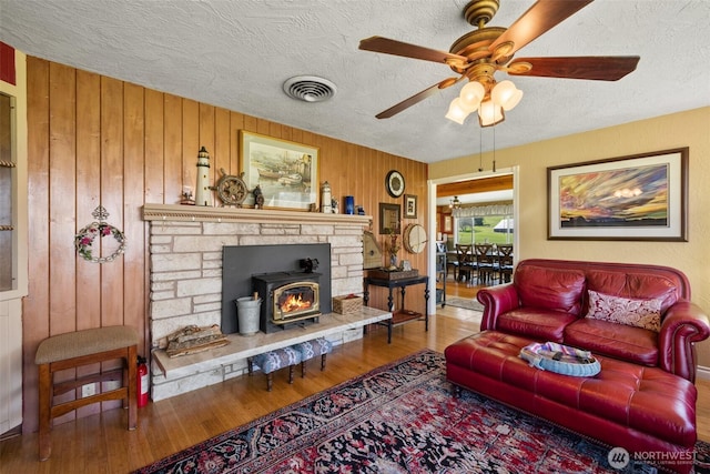 living area with a textured ceiling, visible vents, a ceiling fan, wood finished floors, and wooden walls