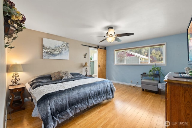 bedroom with a barn door, wood finished floors, baseboards, and ceiling fan