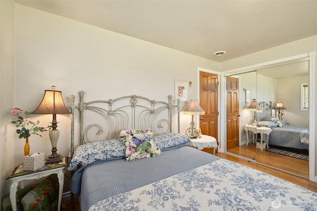 bedroom with wood finished floors, visible vents, and a closet