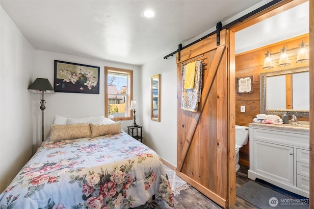 bedroom with a barn door, recessed lighting, wood walls, wood finished floors, and baseboards
