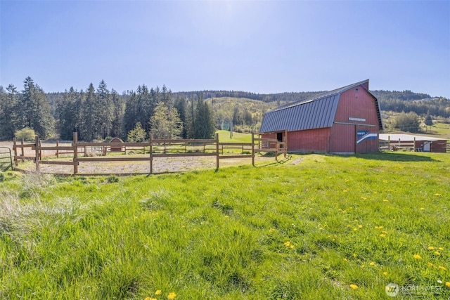 view of yard featuring a view of trees, an outbuilding, a barn, and fence