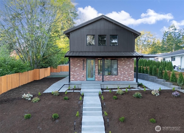 contemporary home with fence, board and batten siding, covered porch, brick siding, and metal roof
