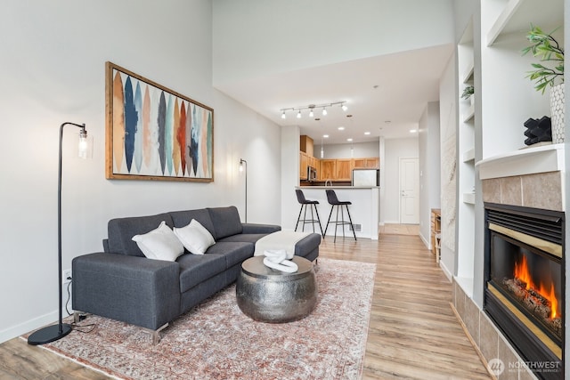living room with baseboards, a tiled fireplace, built in features, and light wood-type flooring