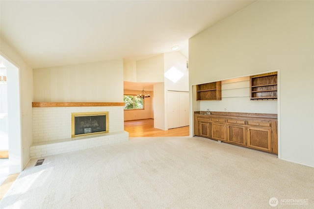169 Fairway Dr, Sequim, WA 98382 - unfurnished living room with light carpet, visible vents, a chandelier, lofted ceiling, and a brick fireplace