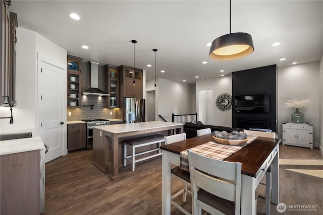 kitchen featuring wall chimney range hood, tasteful backsplash, glass insert cabinets, appliances with stainless steel finishes, and dark wood-style flooring