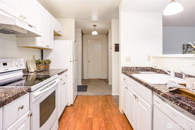 kitchen with dark countertops, a sink, white appliances, and light wood-type flooring