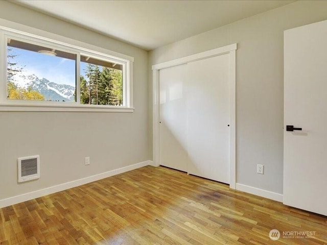unfurnished bedroom featuring a closet, wood finished floors, visible vents, and baseboards