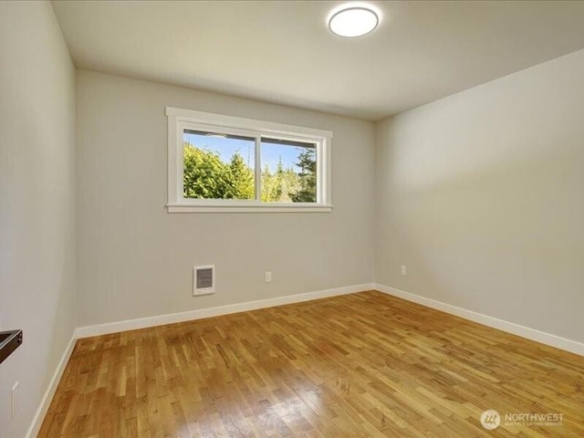 spare room featuring light wood-type flooring, visible vents, and baseboards
