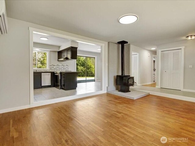 unfurnished living room with light wood finished floors, baseboards, and a wood stove