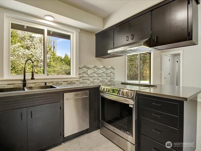 kitchen featuring a sink, light tile patterned floors, stainless steel appliances, a peninsula, and under cabinet range hood