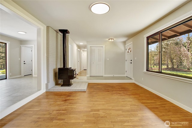foyer with light wood finished floors, baseboards, and a wood stove