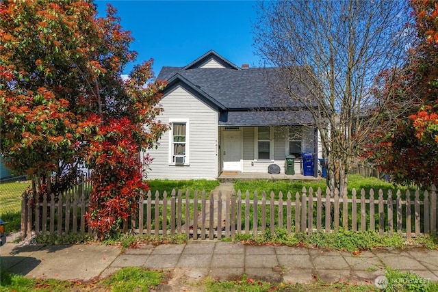 bungalow-style home with cooling unit, a porch, a fenced front yard, and a shingled roof
