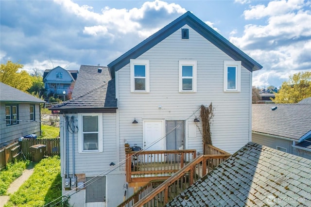 rear view of house with fence and a shingled roof