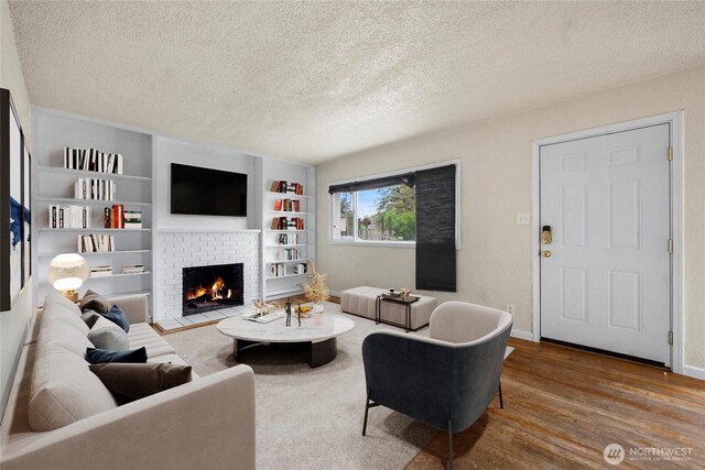 living area featuring a textured ceiling, built in features, a brick fireplace, wood finished floors, and baseboards