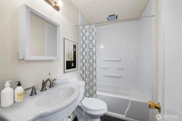 bathroom featuring a sink, a textured wall, toilet, and shower / bath combination with curtain