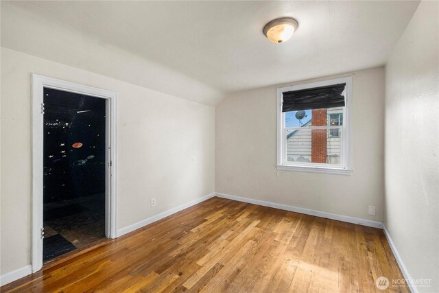 empty room featuring light wood-style floors, baseboards, and vaulted ceiling