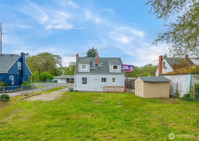 rear view of property featuring fence, a storage unit, an outbuilding, a chimney, and a lawn