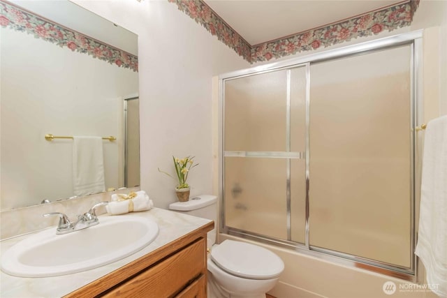 bathroom featuring toilet, combined bath / shower with glass door, and vanity