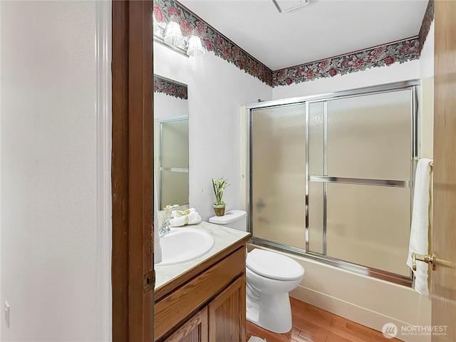 bathroom featuring wood finished floors, shower / bath combination with glass door, vanity, and toilet