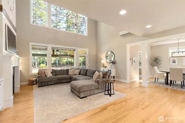 living area featuring an inviting chandelier, a wall unit AC, light wood-style flooring, baseboards, and recessed lighting