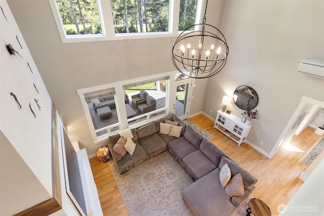 living room featuring wood finished floors, a wall mounted AC, an inviting chandelier, a towering ceiling, and baseboards
