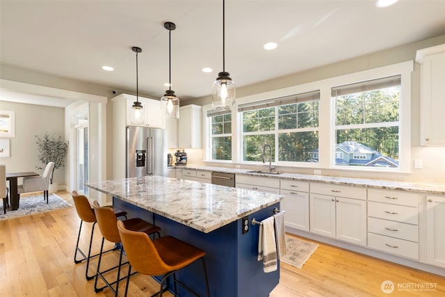 kitchen featuring white cabinets, light stone counters, a sink, light wood-style floors, and appliances with stainless steel finishes