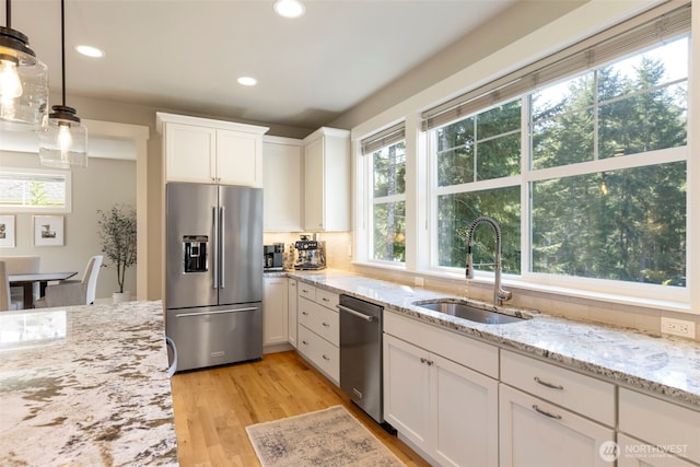 kitchen with white cabinets, a sink, light wood-type flooring, light stone countertops, and appliances with stainless steel finishes