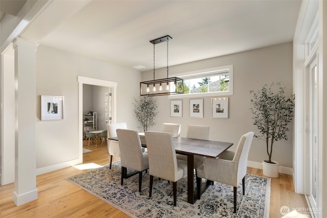 dining room featuring light wood-style flooring, ornate columns, baseboards, and an inviting chandelier
