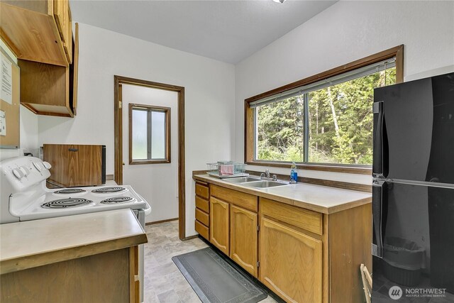 kitchen featuring freestanding refrigerator, a sink, white electric range oven, light countertops, and brown cabinets