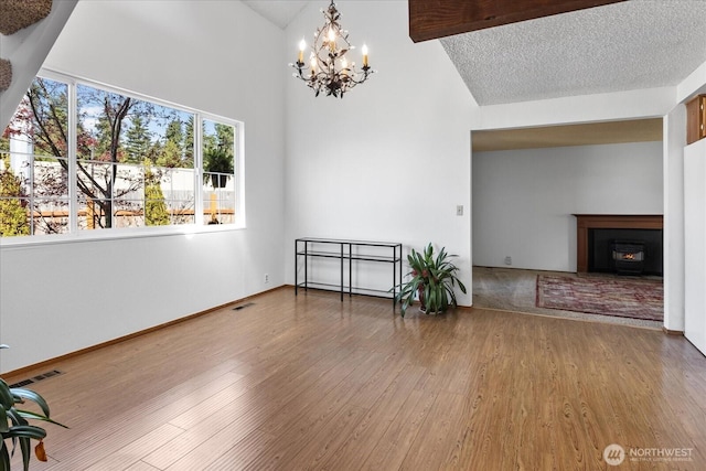 unfurnished dining area with a warm lit fireplace, wood finished floors, visible vents, and a notable chandelier